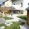 Garten mit Steinen, Holzhaus, Tisch, Hängematte und Sonnenschirm.