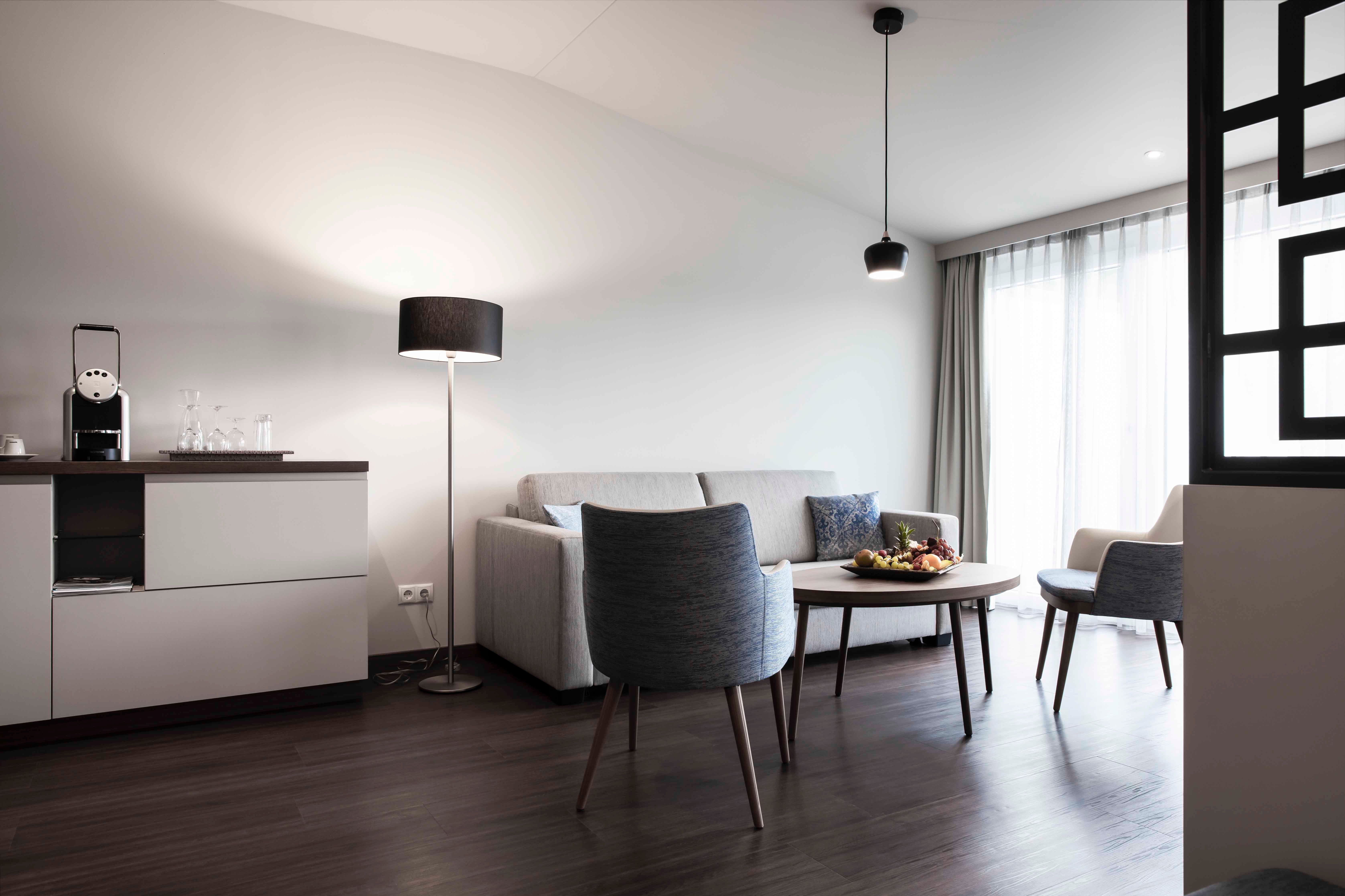 Moderne Sitzecke mit Sofa, Sessel, Tisch und Stehlampe in einem hellen Raum.