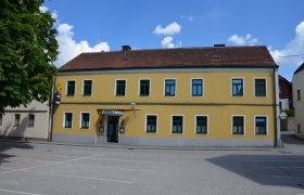 Gelbes zweistöckiges Gebäude mit grünen Fensterrahmen und einem Schild mit der Aufschrift 'Gasthaus Georg Hacker'.