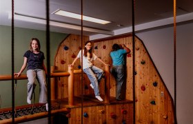 Kinder spielen in einem Indoor-Kletterbereich mit Holzwänden und bunten Klettergriffen.