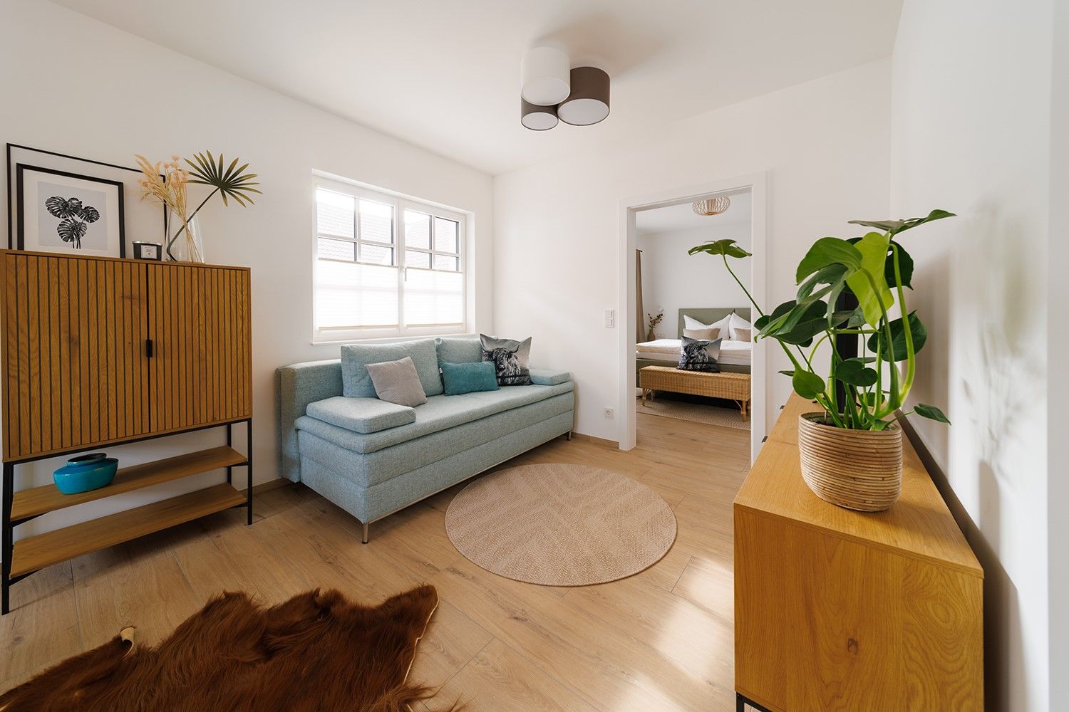 Modernes Wohnzimmer mit hellblauem Sofa, Holzmöbeln und Zimmerpflanze.