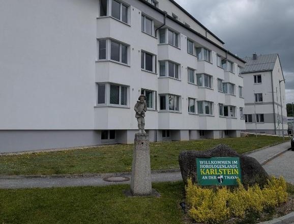 Ein modernes, weißes Gebäude mit mehreren Stockwerken und einem Schild mit der Aufschrift 'Willkommen im Horologenland Karlstein an der Thaya'.