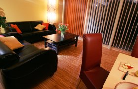 Gemütliches Wohnzimmer mit Ledersofas, Couchtisch, Blumenstrauß und Esstisch mit Obst.