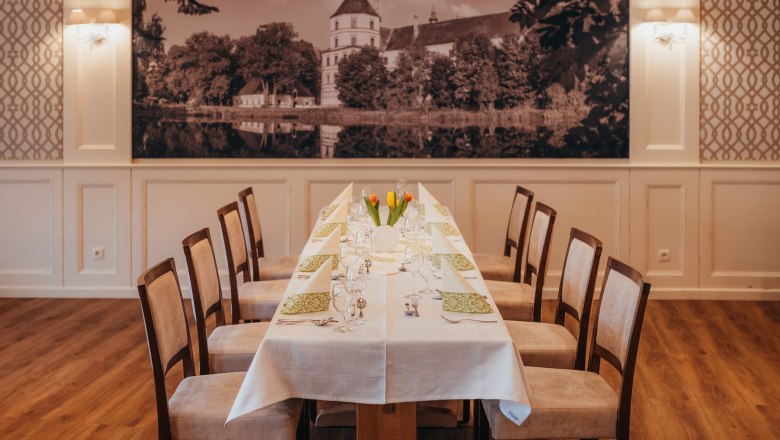 Elegant dining room with a long table, laid with white tablecloths and green napkins, with a large picture of the castle in the background.