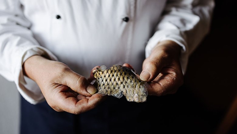 Person in weißem Kochmantel hält ein Stück Fischhaut in den Händen.