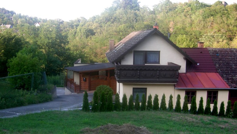 Ein Haus mit Balkon und Garten, umgeben von Bäumen und Hügeln.