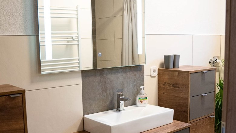 Modernes Badezimmer mit Holzschränken, Waschbecken und Spiegel.