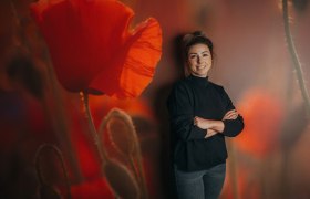 Frau steht vor einer Wand mit Mohnblumenmotiv.