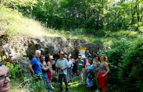 Gruppe von Menschen vor einer Höhle im Grünen.